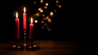Red candles burning in brass candlesticks with warm bokeh lights creating romantic atmosphere on wooden surface against dark background for celebrations.