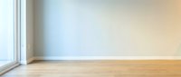 Empty modern room interior with large window, light blue wall, wooden floor and natural sunlight creating warm atmosphere for home design projects.