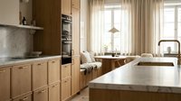 Modern kitchen with natural wood cabinetry, marble countertops, and large windows with sheer curtains. Ideal for home design, interior decoration, and lifestyle publications.