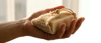 Hand holding natural organic soap bar on a sisal exfoliating pad, eco-friendly skincare concept for wellness and sustainable beauty blogs.