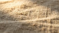 Close-up of natural burlap fabric texture with warm sunlight casting shadows across woven fibers, suitable for backgrounds and textile design projects.