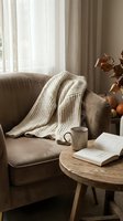 Cozy autumn living room with knitted blanket on sofa, coffee mug and open book on wooden table, warm natural lighting for home decor and lifestyle content.