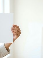 Hand holding blank white card or paper against neutral background, suitable for advertising, marketing campaigns, and promotional materials.