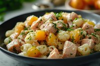Warm potato salad with salmon chunks, yellow cherry tomatoes and fresh dill in black ceramic bowl, close up view of homemade meal with fresh herbs.