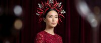 Asian woman wearing elaborate red sequined gown and ornate spiked crown headdress, posed against dark burgundy backdrop with bokeh lighting effects for fashion, editorial, or fantasy portrait use.