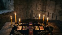 Mystical tarot card reading setup with burning candles on wooden table in atmospheric dungeon setting for fortune telling and divination practices.