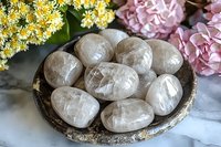Polished rose quartz crystals on rustic wooden plate with pink hydrangea and yellow flowers, healing stones arrangement on marble surface.