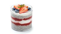 Layered chia pudding with fresh strawberries and blueberries in glass jar, healthy breakfast dessert with yogurt and berries on white background.