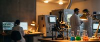 Modern laboratory workspace with microscope and colorful chemical solutions in glass beakers, scientists working in background for research projects.