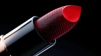 Vibrant red lipstick bullet with textured pattern detail against dark background, dramatic lighting highlights luxurious cosmetic design for beauty and makeup concepts.