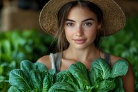 Young woman with olive complexion and long dark hair wearing straw hat holding fresh green leafy vegetables in garden setting for agricultural and farming concepts.