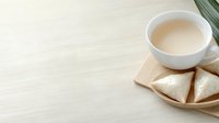 White ceramic cup with milk tea and triangle sandwiches on wooden plate against light background, minimalist breakfast composition with copy space.