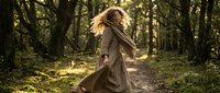 Young woman with flowing blonde hair dancing freely in sunlit forest wearing earth-tone dress, expressing joy and connection with nature in golden hour light.