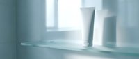 White cosmetic tubes and containers on clean bathroom shelf with soft natural lighting for skincare product mockup and branding design.