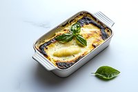 Homemade cannelloni pasta with ricotta cheese and spinach filling baked in creamy sauce, garnished with fresh basil leaves in white ceramic baking dish.