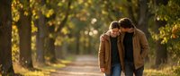 Young couple walking together on tree-lined path in warm autumn light, romantic outdoor lifestyle moment for relationship and love concepts.