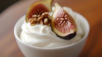 Fresh ripe fig slices and walnuts garnish creamy white yogurt dessert in ceramic bowl, shallow depth of field creates soft background focus.