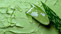 Fresh aloe vera leaf with water drops on textured green background, natural skincare concept showing raw plant extract and moisturizing properties.