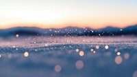 Magical winter snow crystals sparkling in sunlight with blurred mountain silhouettes and soft bokeh effect creating dreamy atmospheric landscape at sunset.