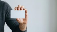 Close-up of male hand holding blank white business card against neutral background, suitable for corporate branding and professional identity mockups.