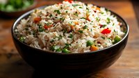 Fluffy white rice garnished with fresh herbs, colorful bell peppers, and seasonings served in dark ceramic bowl on wooden surface, appetizing meal presentation.