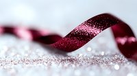 Elegant burgundy ribbon with sparkling glitter scattered on light surface creates romantic festive mood. Curled satin decoration for gift wrapping and holidays.