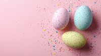 Pastel colored Easter eggs with speckled pattern on pink background with scattered colorful confetti. Festive spring holiday celebration composition.
