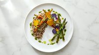 Gourmet herb-crusted fish fillet with colorful edible flowers, microgreens and asparagus on white plate for fine dining restaurant menu presentation.
