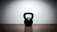 Black kettlebell weight on wooden floor against white wall, suitable for fitness, gym, and workout design projects.
