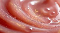 Shimmering pink cosmetic cream with golden particles and smooth swirls, macro shot showing luxurious texture for skincare advertising.