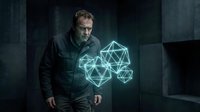 Mature man with glasses wearing dark jacket stands beside glowing geometric neon wireframe shapes in industrial concrete setting, representing technology, innovation, and digital transformation concepts.