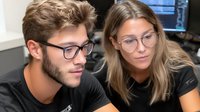 Young Caucasian male and female professionals with glasses collaborating on computer work in modern office environment for business teamwork projects.
