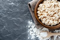 Fresh cottage cheese in wooden bowl on dark stone background with scattered salt and wooden spoon, top view with copy space for text.