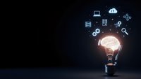 Glowing light bulb with brain inside surrounded by floating technology icons on dark background representing innovation and creative thinking in business.