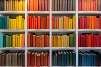 Colorful bookshelf with books arranged by color spectrum from green and yellow to orange and red, creating vibrant rainbow pattern in library.