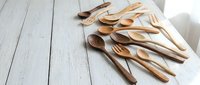 Wooden kitchen utensils set with spoons, forks and spatulas on white wooden table background for cooking and food preparation.