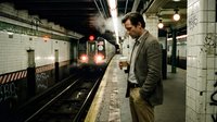 Professional businessman in suit waiting on subway platform as train arrives at underground station during evening commute in urban transit system.