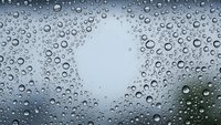 Water droplets on glass surface creating natural rain pattern with blurred background for weather and seasonal concepts.