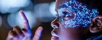 Young African woman with glowing blue glitter makeup in profile view against dark background with bokeh lights, holding illuminated finger creating magical atmosphere.