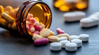 Colorful prescription medication pills and tablets spilling from amber bottle on dark surface, dramatic lighting highlights pharmaceutical drugs and capsules.