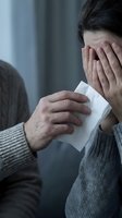 Caring person offering tissue to a crying woman covering her face, expressing grief, sadness, and emotional support in a comforting moment.