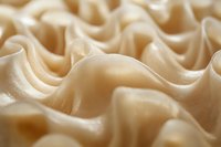 Soft waves of cream-colored meringue create abstract curves and shadows in macro photography, showing delicate texture and smooth flowing patterns in light beige tones.