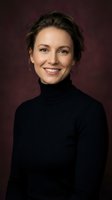 Professional Caucasian woman in black turtleneck smiling warmly at camera against burgundy background. Corporate headshot for business profiles.