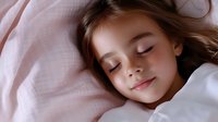 Young girl sleeping peacefully in soft pink bedding with gentle natural light, long brown hair spread on white pillow, serene expression showing sweet dreams.
