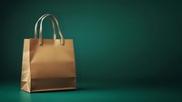 Golden luxury shopping bag with leather handles on dark emerald green background with dramatic lighting and copy space for retail promotions.