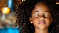 Young African American girl with curly natural hair and closed eyes expressing serenity and peace against soft bokeh background, wellness and mindfulness concept.