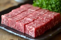 Fresh marbled beef slices arranged on dark plate with green garnish, showing premium meat texture and natural fat marbling pattern for gourmet cooking.