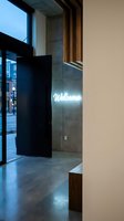 Glowing neon welcome sign on concrete wall in modern building lobby with wood accents, glass entrance, and city street view at dusk.