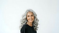 Mature woman with long gray wavy hair, warm smile, wearing black top, isolated on white background for portrait and lifestyle design use.