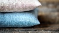 Soft decorative pillows in white and turquoise blue stacked on wooden surface with shallow depth of field creating cozy home atmosphere.